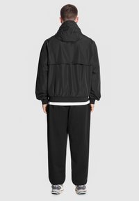 Czarna kurtka przeciwwiatrowa z kapturem, elastycznymi mankietami i pasem. Połączona z luźnymi czarnymi spodniami i sneakersami. Prosty design.