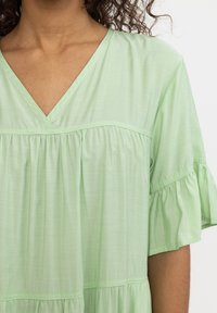 Haut vert clair à manches courtes avec décolleté en V, doté d'un design froncé et d'un tissu texturé pour plus de profondeur.