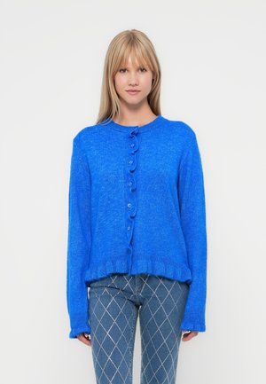 Blauwe gebreide cardigan met een ronde halslijn, voorzien van een knopenfront en golvende rand. De mouwen zijn lang met ribgebreide manchetten.