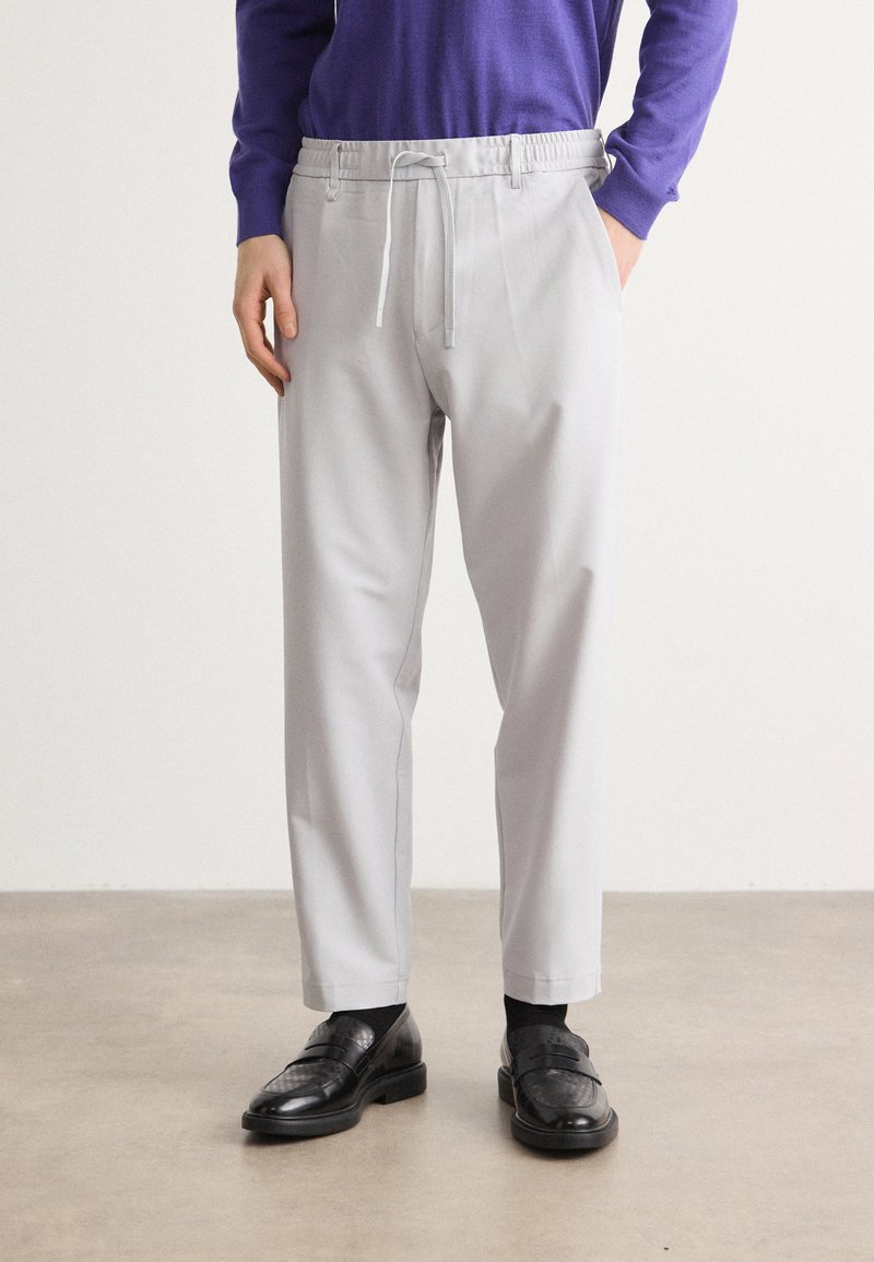 Hellgraue Hose mit elastischem Bund und Kordelzug. Sie bietet einen lockeren Sitz und gerade Beine, kombiniert mit schwarzen Loafers.