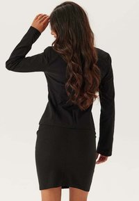 Svart figursydd kavaj med långa ärmar, skräddarsydd design och strukturerade axlar, i kombination med en matchande figurnära svart kjol.