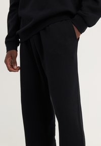Pantalons de survêtement noirs en tissu doux avec une coupe décontractée. Comprend des poches latérales et une taille plate avec des détails de couture subtils.