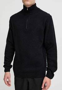 Pulover negru din tricot cu guler înalt și închidere cu fermoar pe jumătate. Prezintă manșete și tiv din material rib. Textură moale, croială relaxată, branding minim.
