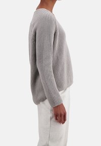 Pull gris en tricot à coupe ample, avec une texture côtelée et des fentes sur les côtés. Il possède des manches longues et un large col rond.