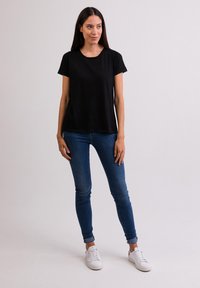 Sort kortærmet t-shirt med rund halsudskæring, parret med blå skinny jeans og hvide sneakers, båret af en model mod en ensfarvet baggrund.