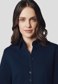 Granatowa koszula z guzikami, wykonana z teksturowanej tkaniny, z kołnierzykiem i widoczną zapinana na guziki, prezentująca strukturalny krój.