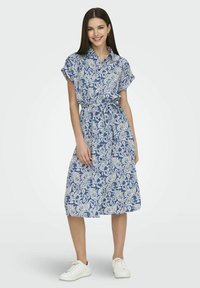 Vestito blu e bianco con motivo paisley, colletto, maniche corte, cintura in vita e lunghezza al ginocchio, abbinato a sneaker bianche.