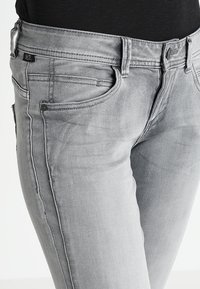 Jeans de mezclilla gris con un corte ajustado, que cuentan con cinco bolsillos, un sutil desgastado y un acabado desvaído. Costuras negras a lo largo de las costuras laterales.