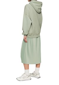 Lichtgroene oversized hoodie met een capuchon, gecombineerd met een geplooide midirok in dezelfde kleur. Witte sportsneakers maken de look compleet.