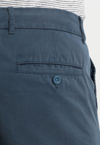 Shorts en coton bleu marine avec une poche latérale, une fermeture par bouton et un détail de couture contrastant le long de la poche et de la taille.