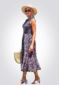 Vestido negro sin mangas con estampado floral que presenta un corpiño ajustado y una falda fluida. Combinado con un sombrero de paja, gafas de sol y un bolso de mimbre.