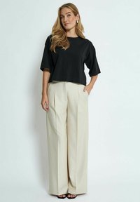 Zwarte cropped t-shirt van zachte stof gecombineerd met beige hoge geplooide broeken. Inclusief een zijzak en elegante zwarte sandalen.