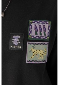 Tessuto nero con tre toppe colorate: una con uccelli in viola e verde, un'altra con un animale maculato giallo e un logo di marca.