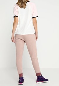 Rosa och vit kortärmad skjorta med svarta detaljer, ihop med ljusrosa sweatpants. Outfiten fulländas med lila träningsskor.