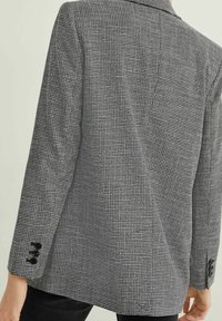 Blazer de patrón de espiga en blanco y negro, diseño estructurado, con dos botones en cada puño, tejido texturizado y corte entallado.