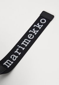 Sangle tissée noire portant le mot "marimekko" en lettres blanches contrastées ; comprend une surface texturée et un matériel rectangulaire plat.