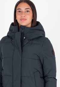 Diepblauwe pufferjack met een capuchon, voorzien van een ritssluiting, zijzakken en een logo patch op de mouw. Glad, geïsoleerd materiaal.