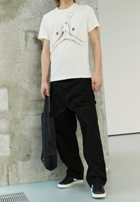 Vit bomulls-T-shirt med en svart Jordan-logotyp och texten "AIR", sammanställd med svarta cargobyxor. Svart tygväska och svarta sneakers.