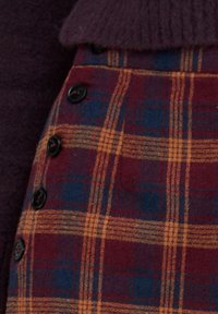 Karierter Rock in Weinrot, Blau und Senfgelb mit strukturierter Stoffqualität. Mit schwarzen Knöpfen an der Seite. Klassisches Karomuster.