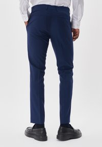 Jūros mėlynumo slim-fit kelnės su lygiu paviršiumi, turinčios užpakalines kišenes ir pritaikytą dizainą, derinamos su juodais loafer'iais.