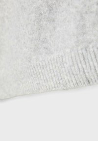 Tissu tricoté gris clair avec un ourlet côtelé, présentant une texture douce et duveteuse.