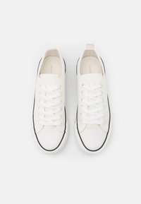 White canvas sneakers with black rubber accents. Features round toe, flat laces, and textured sole. Simple design with no additional patterns.