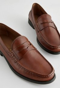 Brune læder loafers med en glat, poleret overflade, der har dekorativ syning og en sort gummisål. Klassisk slip-on design.