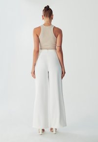 Beige žebrovaný top na ramínka v kombinaci s bílými kalhotami s vysokým pasem a širokými nohavicemi. Oblečení se pyšní čistým, minimalistickým designem s hladkou texturou.