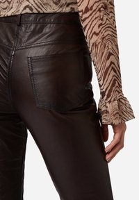 Bruine leren broek met een gladde textuur en details van een achterzak, gecombineerd met een gestreepte langemouwenshirt met volantmanchetten.