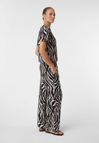 Zebra-Muster-Outfit mit einer lässig geschnittenen Bluse und weiter Beinform in Creme, Schwarz und Burgunderrot, gefertigt aus weichem Stoff mit Taschen. Sandalen inklusive.