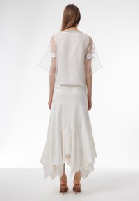 Blusa blanca transparente con flores bordadas, combinada con una falda larga y fluida blanca con volantes en capas. Tela suave y ligera.