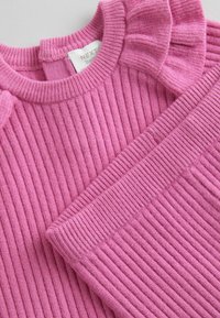 Maglione rosa a coste con scollo rotondo e dettagli arricciati sulle spalle. Realizzato in morbido tessuto, presenta un punto lavorato testurizzato e un design versatile.