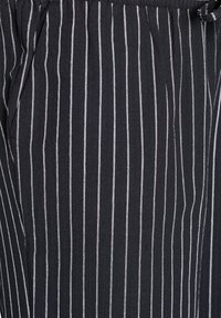 Tessuto nero con strisce bianche verticali, caratterizzato da una consistenza morbida e una vestibilità ampia. Notevole per il suo design casual e la cintura elastica.