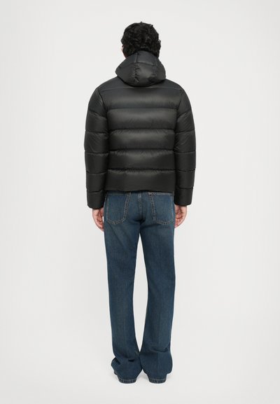 Schwarze Daunenjacke mit Kapuze, ausgestattet mit einem gesteppten Design und glänzender Textur. Kombiniert mit lässigen, weit geschnittenen blauen Jeans.