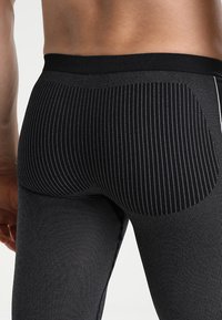Leggings a rayas negras con un diseño ajustado, que presentan una cinturilla en contraste. La textura de la tela parece suave con acanalados verticales.