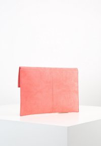 Koralowa skórzana kopertówka o gładkiej fakturze, prostokątnym kształcie i czystych liniach. Posiada złożoną klapę z subtelnym przeszyciem.
