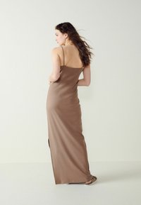 Rochie maxi ajustată, de culoare maro, cu bretele subțiri, având un croi drept și o fanta pe lateral. Textură netedă, design minimalist.