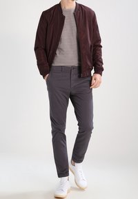 Burggunder bomberjacka över en randig grå t-shirt, kombinerad med grå byxor och vita sneakers, vilket visar en avslappnad, modern stil.