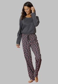 Gray long-sleeve top with scalloped cuffs, paired with dark pajama pants featuring a red and white star pattern and an elastic waistband.