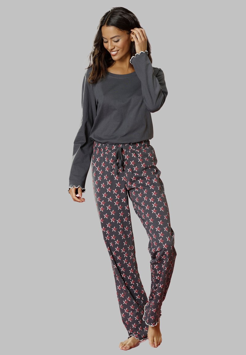 Gray long-sleeve top with scalloped cuffs, paired with dark pajama pants featuring a red and white star pattern and an elastic waistband.