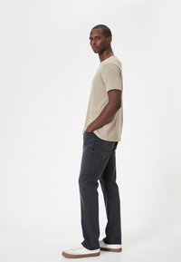 Camiseta de manga corta beige combinada con jeans gris oscuro y zapatillas blancas. Los jeans tienen un diseño de pierna recta y una textura sutil.