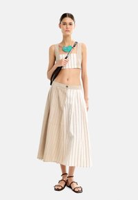 Dwuczęściowy strój z krótką, beżową bluzką w paski oraz długą, beżową spódnicą w czerwone paski. Uzupełniony turkusową naszyjnikiem i brązowymi sandałami.