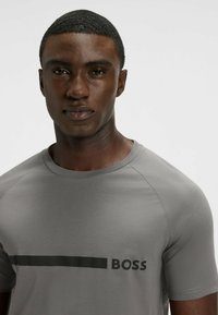 Szara koszulka z okrągłym dekoltem i krótkimi rękawami, z czarnym logo „BOSS” nadrukowanym z przodu. Gładka faktura tkaniny.