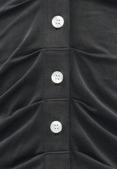 Black, textured fabric top featuring a row of four white circular buttons and gathered detailing along the front seam.