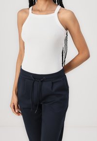 Vit ribbad linne med breda band, kombinerat med mörkblå joggerbyxor med elastisk midja och dragsko.