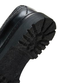 Zwarte sportieve schoen met een gestructureerde rubberen zool met een geribbeld patroon en een stevige leren bovenkant, ontworpen voor verbeterde grip en duurzaamheid.