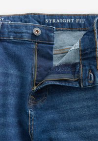 Rechtafstaande denim jeans in donkerblauw, met een ritsluiting, metalen knoop en contrasterende gele stiksels op de zakken en naden.