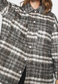 Gelaagd jasje met een kraag, gekenmerkt door een geruit patroon in grijs, wit en bruin, versierd met witte knopen en een borstzak.