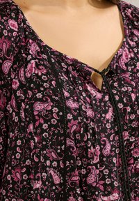 Top nero floreale con motivi paisley rosa, tessuto testurizzato, scollatura a V e dettaglio cucito con un laccio al centro.