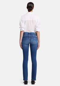 Blå denimjeans med rak bendesign, med bakfickor och hög midja, tillsammans med en vit skjorta med krage.